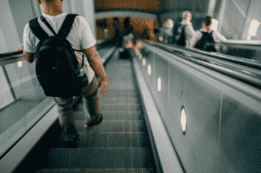 man wearing backpack walking down escalator